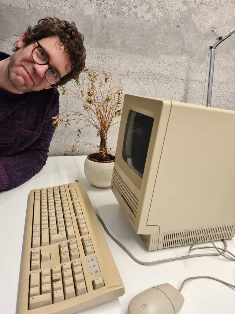 Bastian am alten Apple Rechner mit verwelkter Blume